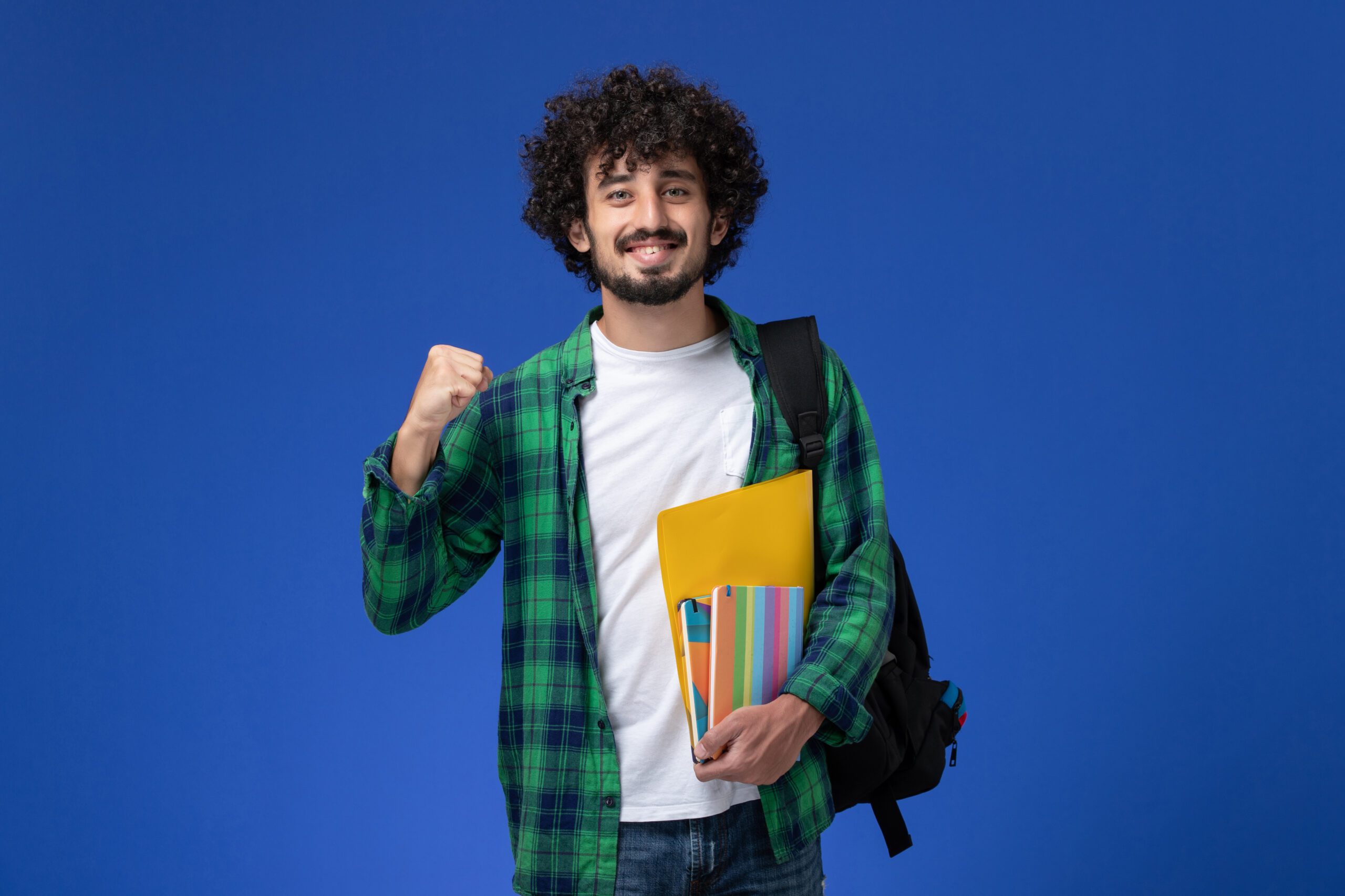 front view male student wearing black backpack holding copybooks files blue wall scaled